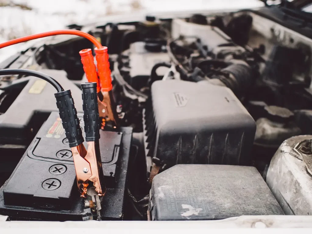 Car battery beside an open battery tray in a repair bay with a mechanic checking fitment