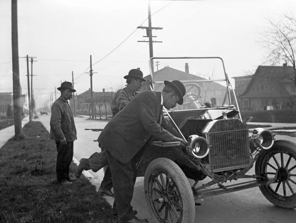 Car owner updates a paper binder and smartphone log at a kitchen table after a service visit.