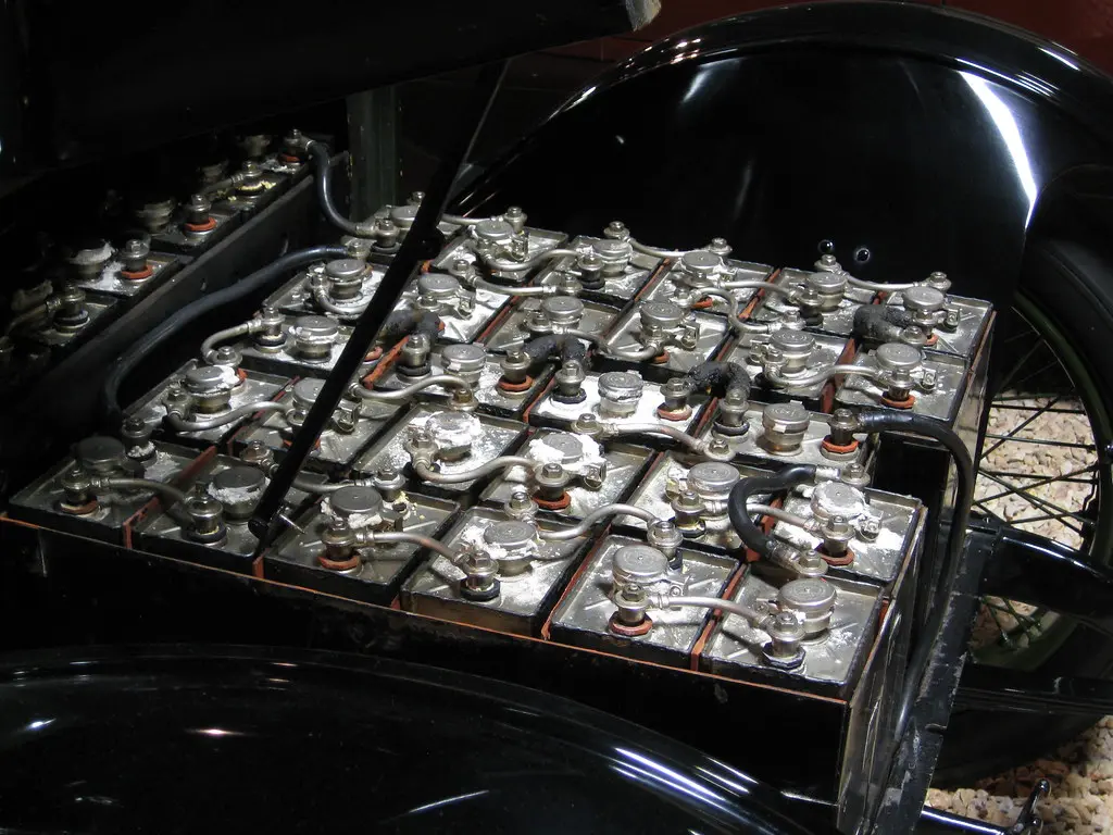 Battery maintainer clips attached to a car battery terminal inside an open hood.