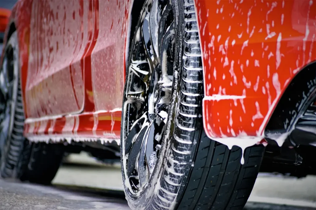 A person washing a silver car with a microfiber mitt beside two buckets in soft daylight.