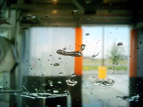 Close-up of a microfiber wash mitt rinsing in a bucket next to soapy water.