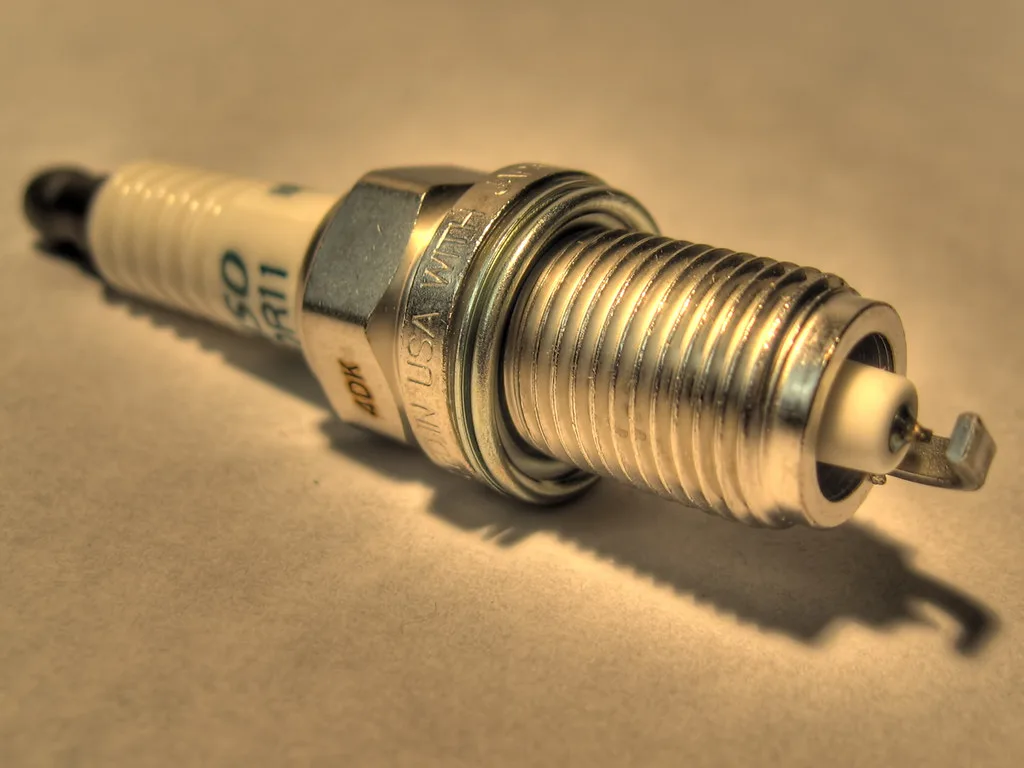 Close-up of an iridium spark plug beside a copper spark plug on a shop towel