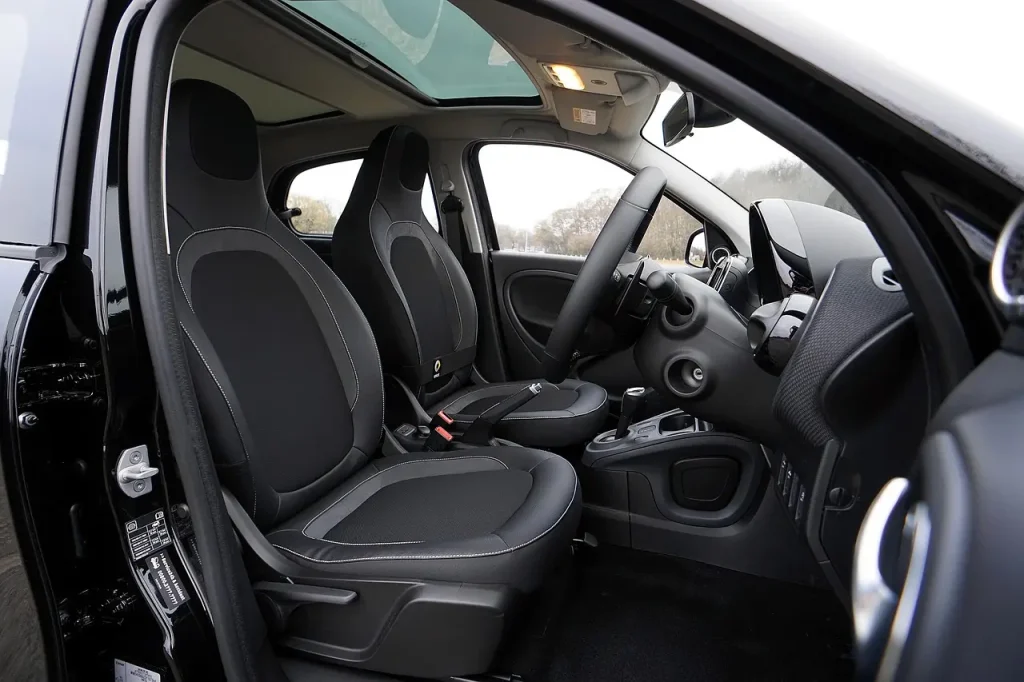 Person cleaning a car interior with vacuum and cloth in natural daylight