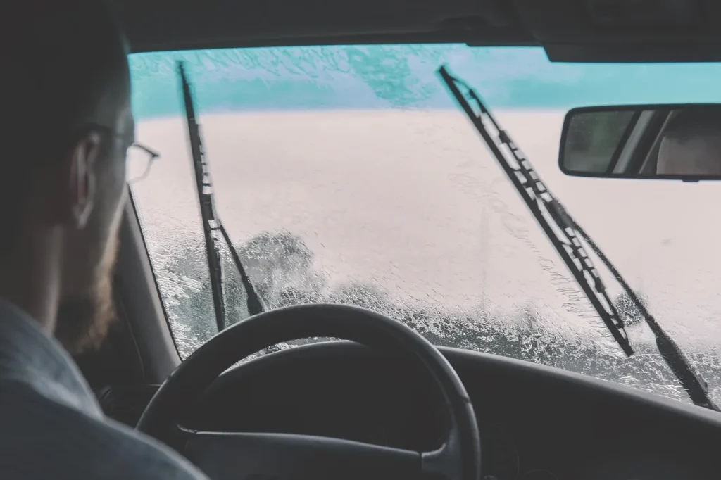 Person comparing windshield wipers and connector types beside a car in daylight