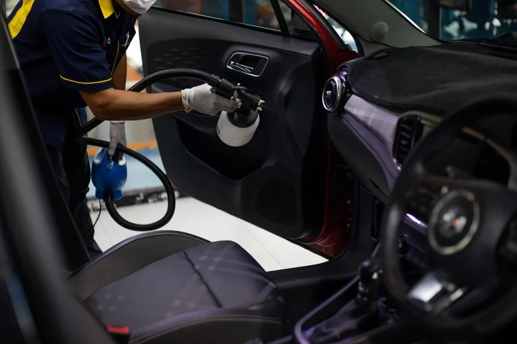 Person wiping a black car interior dashboard and door trim with microfiber cloth in natural light