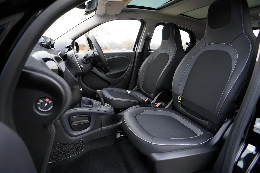 Person vacuuming a car interior with open doors in natural light