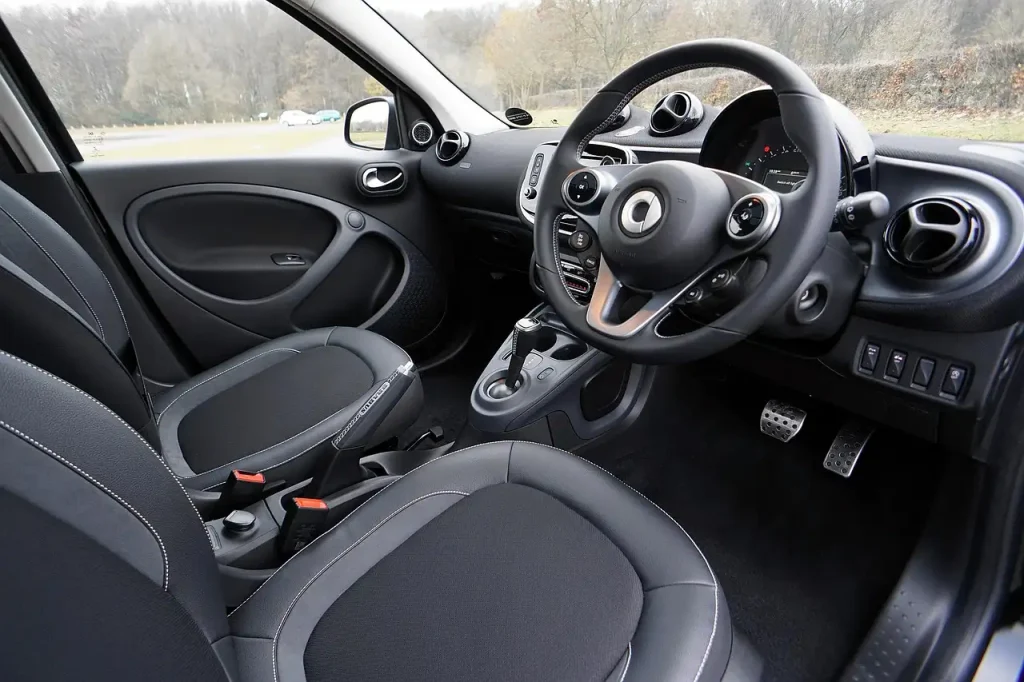 Person wiping a car interior dashboard and console with a microfiber cloth in natural light