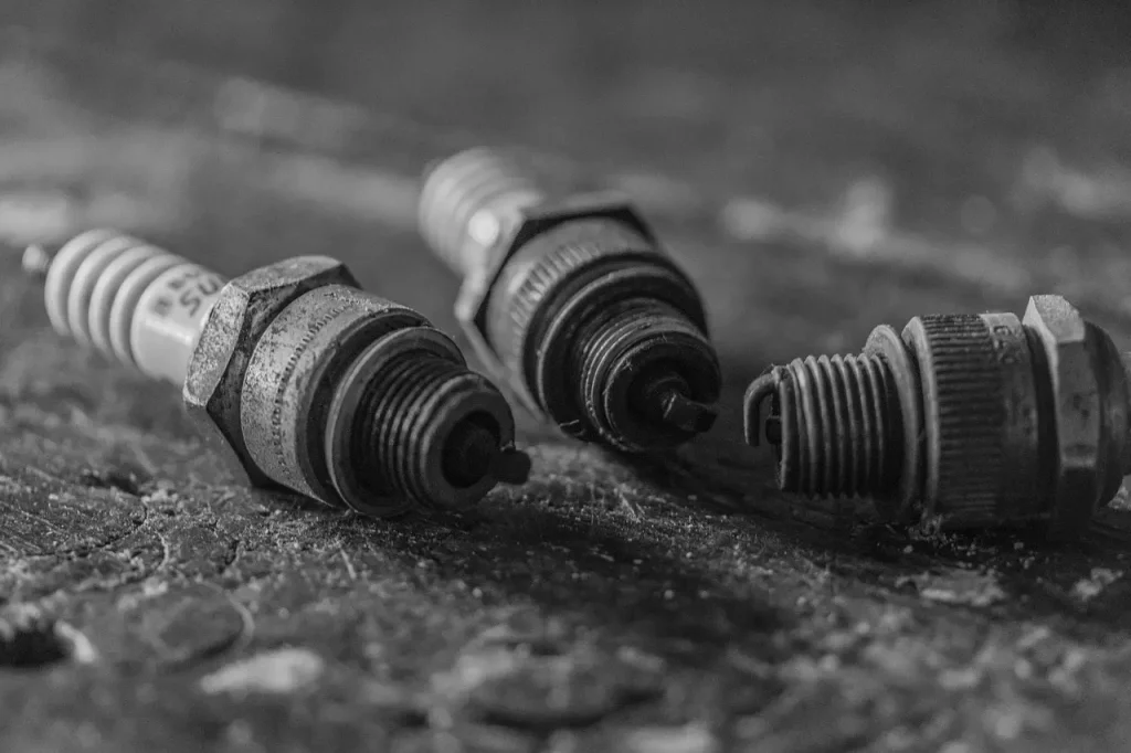 A mechanic inspects fouled spark plugs on a garage workbench with cleaning tools nearby.