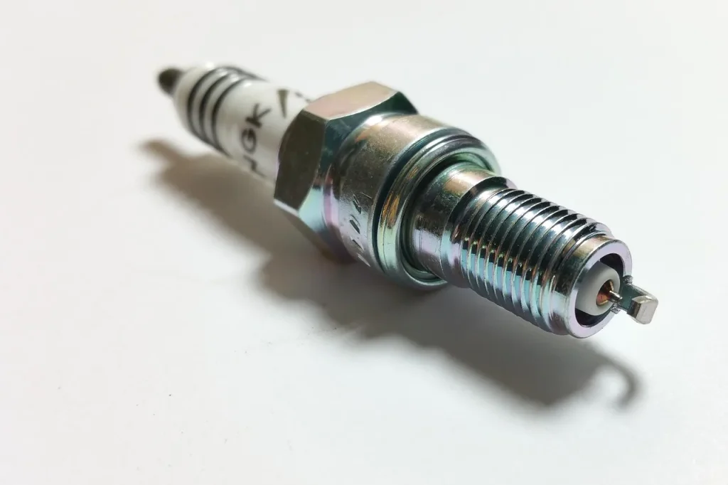 Used spark plugs on a garage workbench with a hand inspecting one under natural light