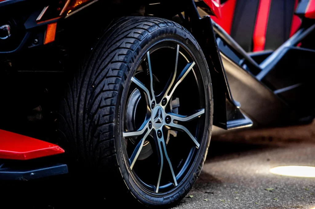 Mechanic holding an alloy wheel beside a car wheel well in a bright garage