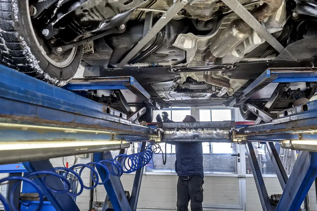 Mechanic inspecting a car's front suspension and control arm area in a repair bay