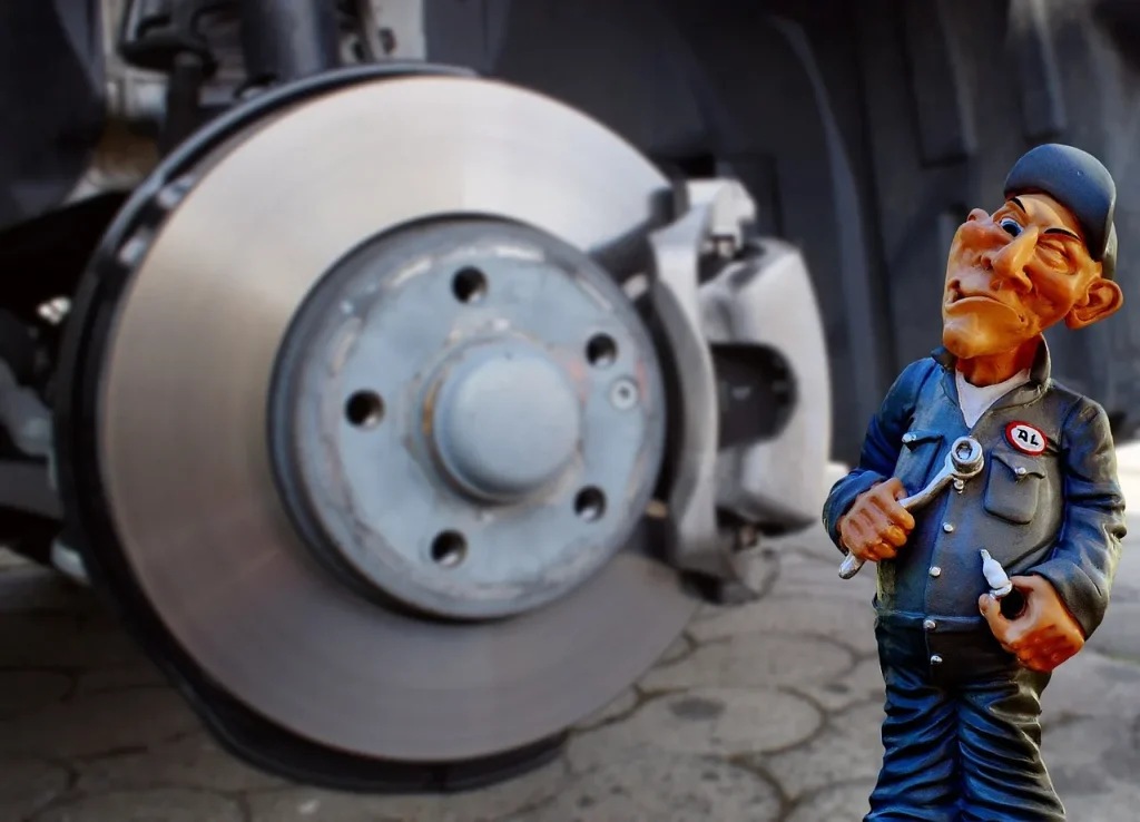Mechanic inspecting brake hardware beside a car with the wheel removed in a garage