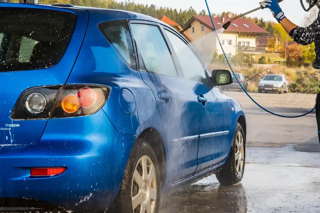 Car paint with water beading as a person rinses a dark sedan in natural morning light