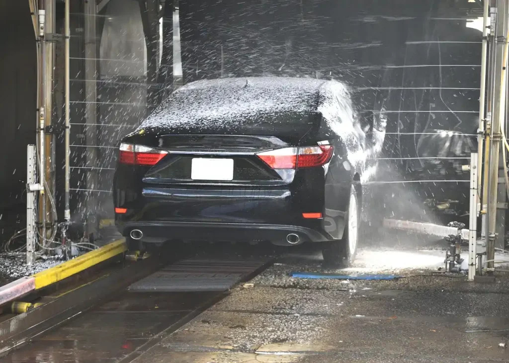Person hand-washing a sedan with bucket and hose in a sunny driveway