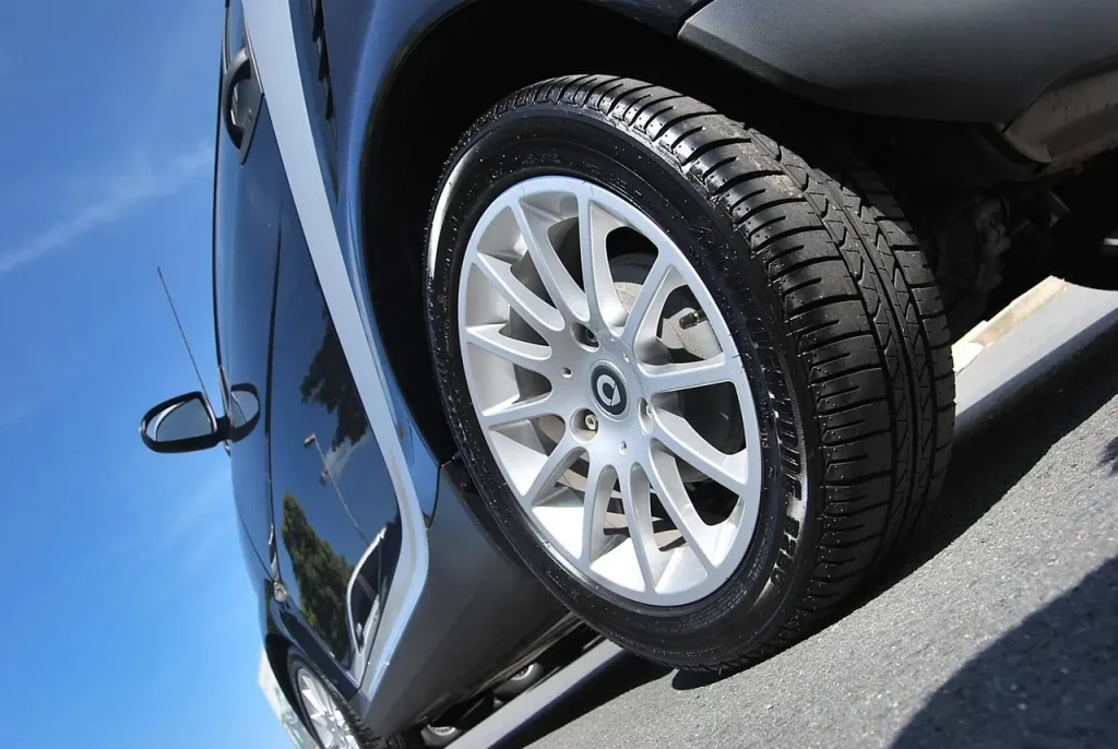 Forged wheels beside a sports sedan in a sunlit garage