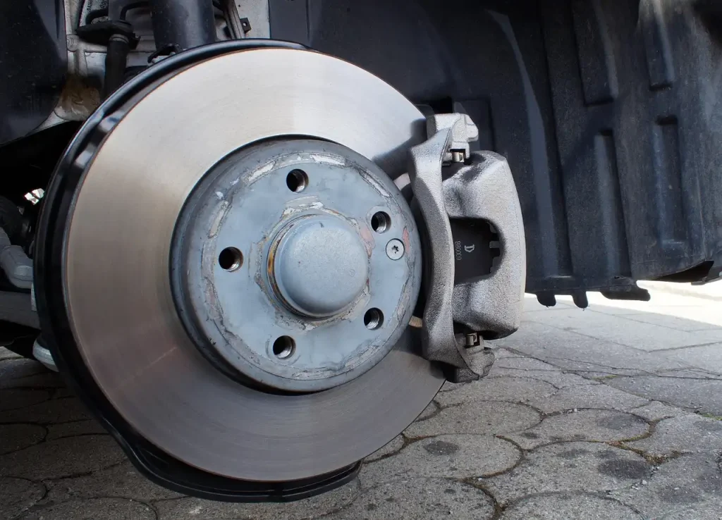 Mechanic inspecting a car brake caliper beside the rotor in a repair bay